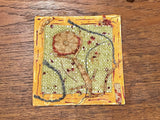 Textured green ground, frayed red fabric flower, dark threads, and gold border on mixed media art.