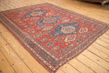 Angled view of an antique Caucasian Soumac carpet, showcasing the intricate geometric medallions on a cherry red field.