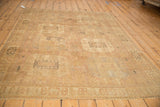Angled view of a distressed Oushak rug with a faded mauve and gold geometric column design.