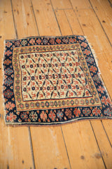 Angled view of an antique Kurdish rug highlighting its geometric trellis design and worn, frayed edges.