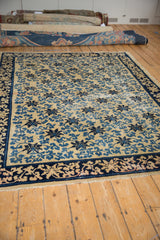 An antique Peking carpet from an angle, showing the texture of wear on its blue lattice and vine design.