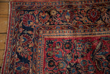 Navy blue border with floral bouquets framing the raspberry red field of an antique Sarouk carpet.