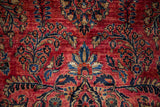 Close-up of hand-knotted floral sprays with scattered white knots on an antique Sarouk's raspberry red pile.