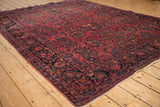 Angled view of an antique Sarouk carpet's navy vine border and raspberry red floral field.