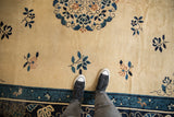 Close view of the antique Peking carpet's low pile, showing its time-softened texture and scattered blue floral motifs.