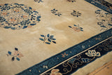 Close-up on bat-like floral motifs and the navy border of an antique Peking rug with a low wool pile.