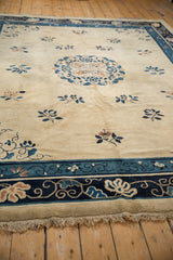 Low angle on an antique Peking carpet, showing the tattered end, navy floral border, and ivory field.