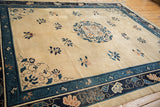 Angled view of an antique Peking carpet showing its ivory field, blue medallion, and floral corner details.