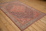 Antique Malayer rug from a high angle, displaying a rose medallion and dense navy Herati pattern.