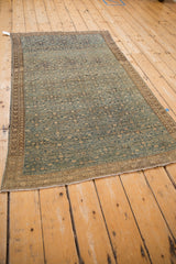 Antique Malayer rug corner, showing distressed field, germinating vine border, and white fringe.