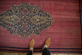 Navy and sand trefoil medallion on the worn raspberry red pile of an antique Persian rug.