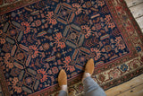 A perspective view of the antique Malayer rug, highlighting stylized animal and human figures on its navy blue field.