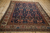 Angled view of antique Malayer rug showing geometric animal motifs and classic lotus vine border.