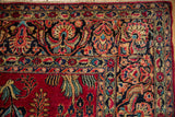 Detailed corner of a vintage Sarouk carpet showing the navy palmette border beside the cherry red field.