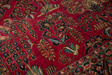 Close-up of palmettes and floral sprays in navy and green on the cherry red, hand-knotted pile of a Sarouk carpet.
