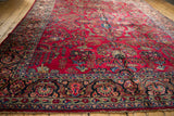 Angled view of a vintage Sarouk carpet's cherry red field and intricate navy blue floral border.