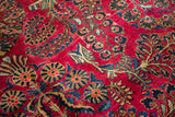 Intricate floral sprays and pinwheel motifs in blue and sand across the short, cherry-red pile of a Sarouk carpet.