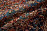 Folded antique Heriz carpet showing textured pile with brick red and sapphire blue geometric motifs.