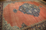 Perspective view of the antique carpet's navy medallion, ivory spandrel, and wide floral border.