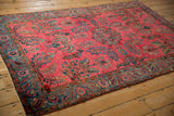Angled view of a raspberry red Sarouk rug with stylized weeping willow and fern patterns.