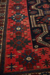 Richly colored geometric floral gul in strawberry red and navy on an antique Persian rug.