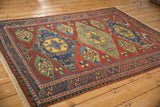 An angled view of an antique Caucasian Soumac rug, showing its bold diamond medallions and complex geometric borders.