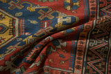 The supple texture of a folded antique Soumac rug, with geometric patterns in ruby red, sapphire blue, and saffron.