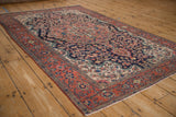 Angled view of an antique Farahan Sarouk rug, highlighting its complex floral pattern and madder red border.
