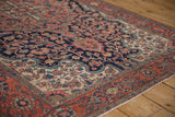 Detailed corner view of an antique Farahan Sarouk rug's madder red border and navy floral field.