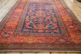 Angled perspective of an antique Hamadan rug's dense Herati field and bold tomato red border.