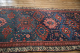 Angled view of an antique Caucasus runner showing the reciprocating wave border and colorful gul medallions.