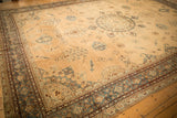 Angled view of an antique Yezd carpet highlights its intricate blue border and distressed sand field.