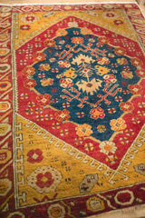 Angled view showing the sapphire medallion, pomegranate red borders, and saffron yellow fields of an antique Anatolian rug.
