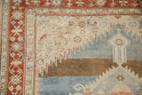 Close-up on the corner of a distressed Karabagh rug, showing animal figures and a madder red border.