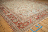 Angled view of a distressed Mahal carpet's terra cotta Herati border and pale green floral field.