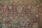 Muted burgundy and teal floral palmettes within the corner borders of a distressed Tabriz carpet.
