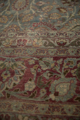 Worn, hand-knotted texture of a vintage Tabriz carpet with floral borders in teal and purple.