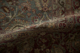 A fold in the distressed Tabriz carpet reveals the dusty teal and burgundy pattern with a soft, low pile.