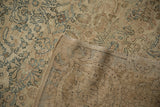 Corner of a distressed Kerman carpet revealing the hand-knotted back and low floral pile.