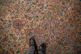 Low pile texture of a distressed Kerman carpet showing sprawling floral designs in sandalwood, sapphire blue, and red.