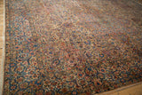 Angled view of a distressed Kerman carpet highlighting the intricate floral and vine border.