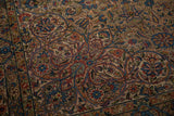 Close-up of interconnected floral vines in blue and red on a vintage distressed Kerman carpet.