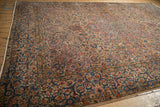 Angled perspective of a vintage Kerman carpet showing its intricate border and sprawling floral field.