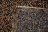 A folded corner of a vintage Kerman rug showing the floral pattern, secured side cord, and short fringe.