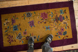 Full view of a vintage Art Deco rug featuring floral sprays on a gold field and a rich aubergine border.