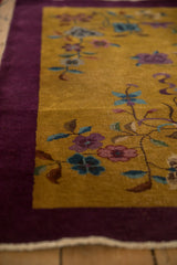 Detail of the vintage rug's corner, showing the aubergine purple border and worn, low pile on the golden field.