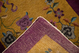 Folded corner showing the aubergine purple hand-knotted back and gold floral pile of a Nichols rug.