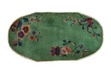 A vintage Nichols Art Deco rug with an oval shape, jade green field, and sparse floral motifs.