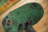 A person's perspective of the oval Nichols Art Deco rug, showing its scale and jade green floral design.