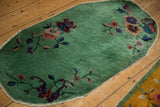 Asymmetrical floral groupings on the jade green field of a vintage Nichols oval rug.